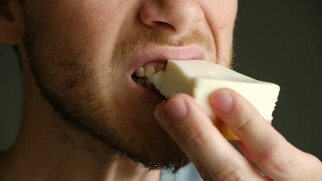 Extreme close up unshaven man mouth taking big bite of slice of sweet cheesecake, chewing with pleasure and enjoyment. Close up of a bearded man eating delicious cheesecake
