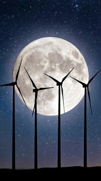 Wind turbines spinning against giant full moon in starry night sky. Lockdown wide shot.