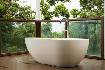 Fototapeta premium White freestanding bathtub on wooden deck with jungle view in resort