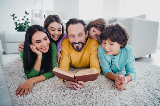 Father reading a book at home with smiling family on the carpet, cozy family bonding moment of togetherness and story time