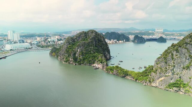 Ha long bay landscape featuring limestone karsts, traditional fishing boats on calm water, and the developing coastline of h long city under a bright sky