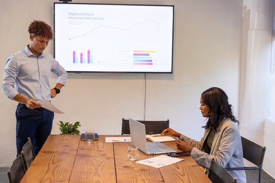 Diverse coworkers discussing digital adoption slide with reports and laptop at conference table