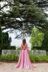 Fototapeta premium Woman in elegant pink gown standing in a historical garden from behind.