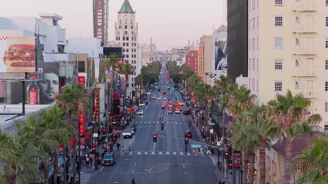 Hollywood Boulevard traffic flowing through Los Angeles with historic buildings, palm trees, illuminated billboards lining bustling urban streetscape