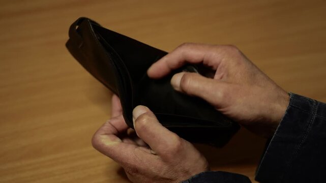 Person's hands examine empty wallet on wooden table at home.