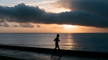 Fototapeta premium A person runs along the coast silhouette against a dramatic sunrise or sunset sky over the sea