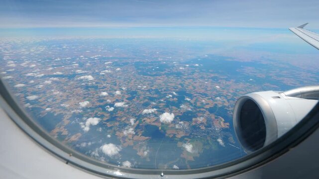 Fly high over agricultural fields at eastern suburbs of Paris, passenger view through airliner window. Cultivated land and small communes seen down, tiny white clouds scattered around