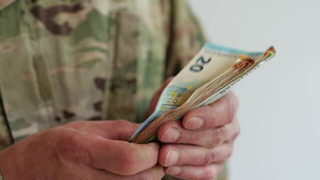 Hand in camouflage uniform counts euro cash and puts money back into pocket