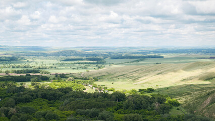 Fototapeta premium Panoramic view of a green valley under an overcast sky showing a grassy hillside with scattered rocks in the foreground sloping into a patchwork of fields