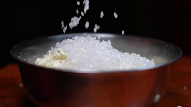 Pouring White Sugar into Fresh Chhena Grains in Metal Bowl Close Up. Adding Sugar to Cottage Cheese Curds for Traditional Indian Sweet Cooking. White Sugar Pouring.