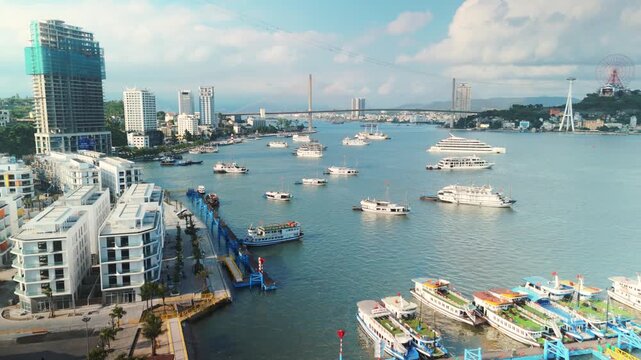 Ha long bay marina with many cruise ships and tourist boats, showing modern high rise buildings, bai chay bridge, and the sun world ferris wheel in h long city, vietnam, on a sunny day
