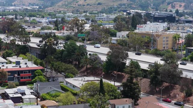 Hollywood freeway traffic with cars driving in Los Angeles, California during day showing apartment buildings and houses alongside Griffith Park mountains