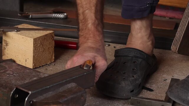 Close up of a metalworker removing a small metal tab with pliers from a steel square tube in a workshop. Precision metal fabrication, finishing process and industrial craftsmanship.