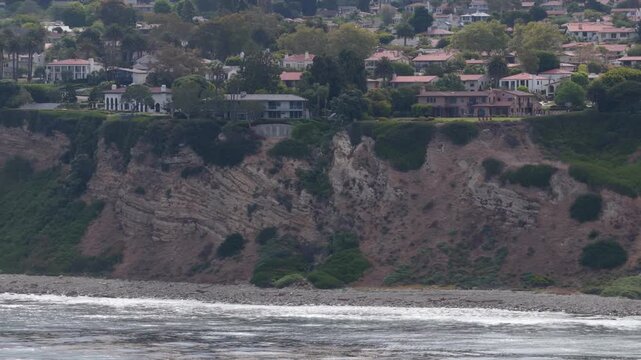 Palos Verdes Peninsula homes on coastal bluffs with ocean waves crashing on shores of Southern California. Upscale residential properties and real estate with sea views