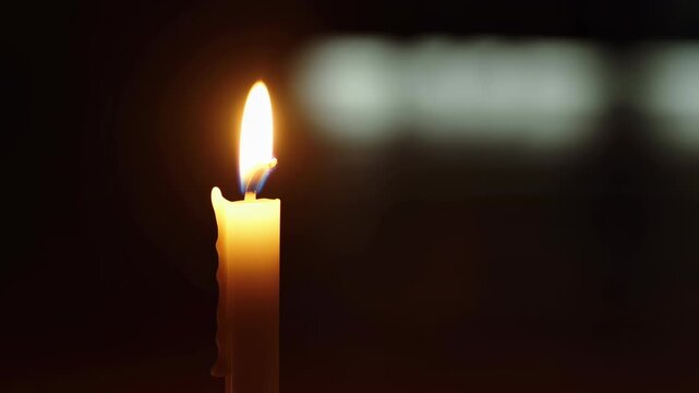 Single burning candle glowing in the dark with bokeh background