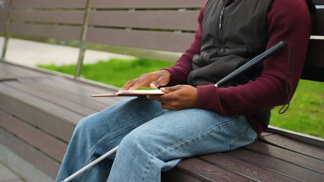 Blind African American man reading a braille book in a park