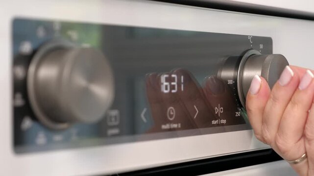 Woman adjusting white oven in kitchen. Female hand pushing and turning knobs on oven control panel. Closeup
