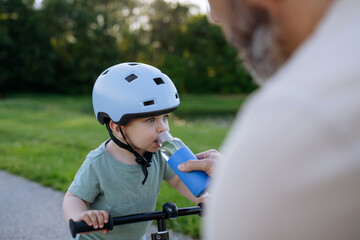 Naklejka premium Father giving water to toddler son during cycling break outdoors.