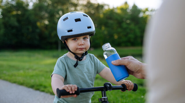 Little boy drinking water from bottle while riding bike in park.
