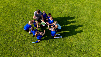 Obraz premium Youth football coaches discussing tactics with players before training.