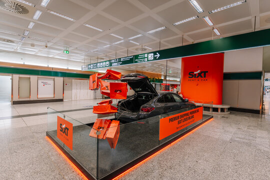 Sixt car rental display featuring a black sedan with open trunk and vibrant orange branding in an airport terminal setting