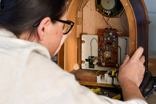 Close up view of a woman examining the interior components of a vintage radio, highlighting repair, maintenance, restoration, electronics, and curiosity about old technology