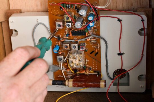 Close up person hand using a screwdriver inside vintage radio, highlighting repair, restoration, maintenance, and retro electronics