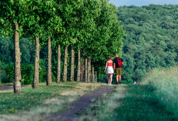 Fototapeta premium Man and woman walking along a beautiful pedestrian tree lined alley path into distance
