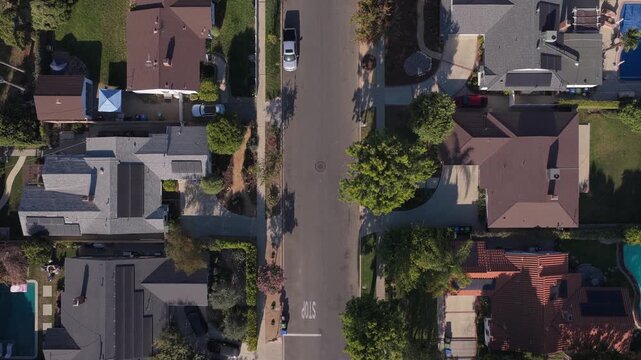 Top down vertical reveal of a Los Angeles suburban neighborhood with houses, cars driving on a street, solar panels, residential backyards with swimming pools