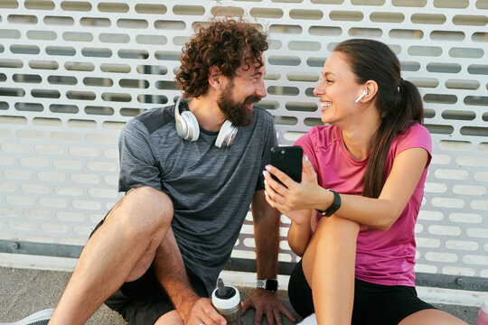 Two individuals take a break from their exercise routine, laughing and sharing fitness tips in a sunny outdoor setting. They are engaged and enjoying each other's company.