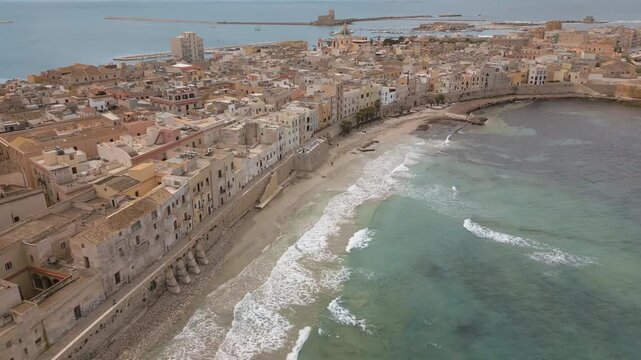 Waves breaking on Trapani Mura di Tramontana sea wall waterfront while seagulls fly past, wide aerial tilt up and pan