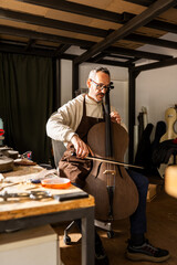 Luthier Plays a Finished Carbon Fiber Cello in Workshop Setting During Daytime © GALDRIC