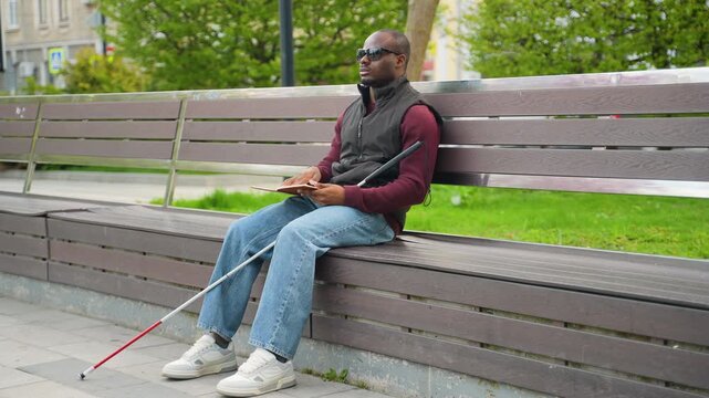Blind African American man reading a braille book in a city park
