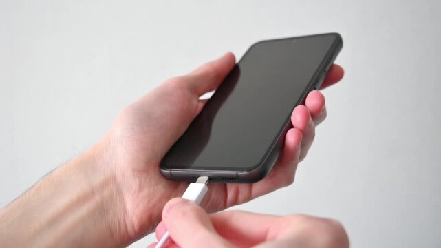 Hands plugging white usb c cable into smartphone showing battery charging screen