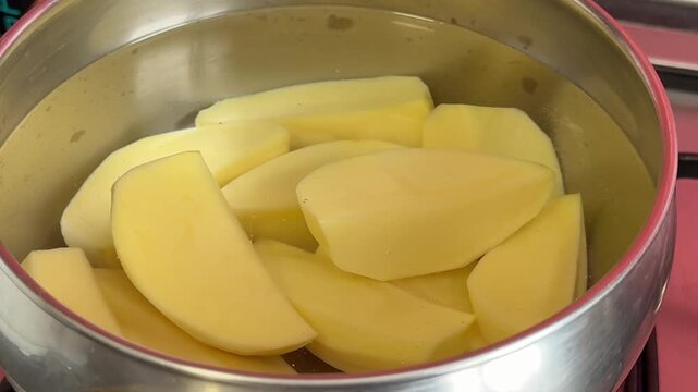 Fresh sliced potatoes soaking in water inside pot while starch slowly releases creating cloudy texture during traditional homemade cooking preparation process.