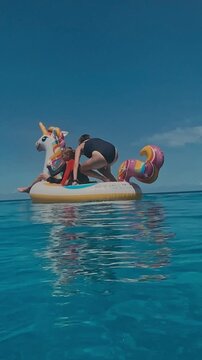 Closeup inflatable unicorn float with boy wearing goggles, turquoise pool water shimmering, sunny sky, playful young snorkeler gripping rim, summer joy and carefree motion, vertical video
