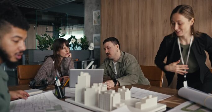Group of architects shares ideas about a building project with models and blueprints during a meeting in an office