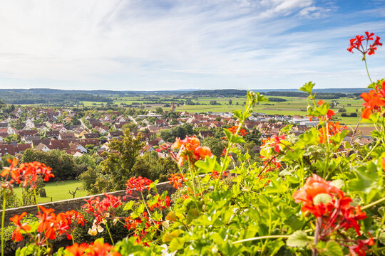 Colmberg, historic small town in region of Bavaria in Germany, Europe. Vibrant Red Geraniums Frame a Picturesque European Village in a Lush Green Valley on a Sunny Day