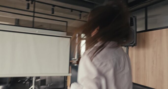 A woman dances in an office environment while music plays in the background, showing enjoyment and energy