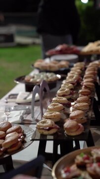 Close-up of a catering reception table featuring rows of mini bagels and sandwiches at an elegant outdoor nighttime event.