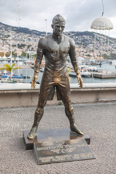 Funchal waterfront in Madeira, tall bronze statue of Cristiano Ronaldo stands on a plaque-adorned pedestal. The athletic monument captures the famous footballer in a powerful standing pose