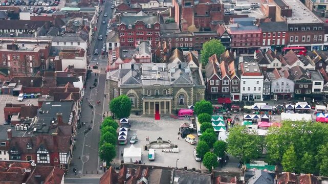 Drone footage looking down over Salisbury Guildhall and Market Square with market stalls historic buildings roads trees and city centre rooftops.