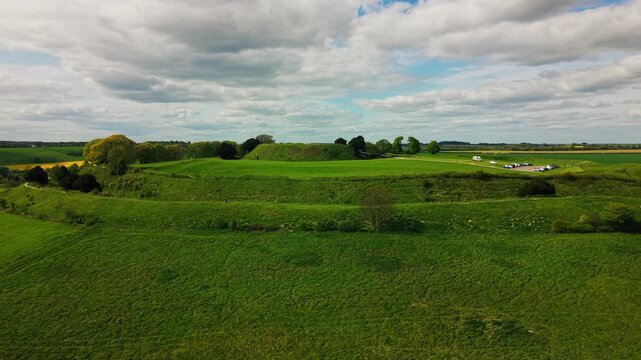 Wide aerial drone view of Old Sarum, the ancient Iron Age hillfort and historic earthwork site near Salisbury in Wiltshire, surrounded by green English countryside, open farmland and dramatic cloudy s