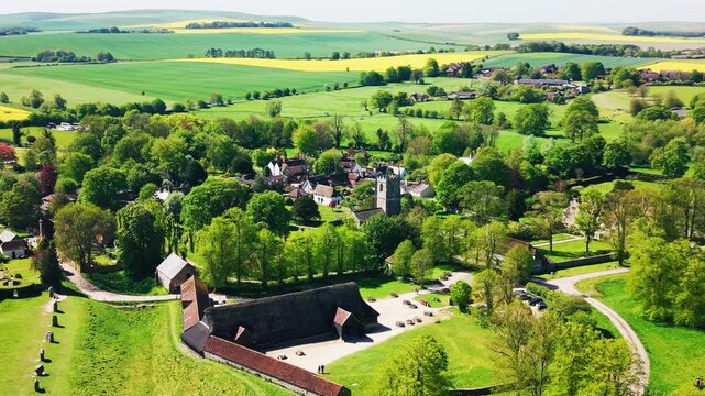 Drone aerial view of Avebury village with a historic church, rural buildings, green trees, farmland and surrounding prehistoric landscape in Wiltshire, England.