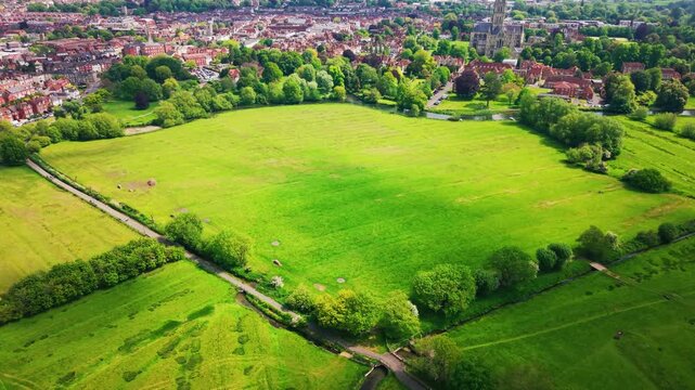 Aerial footage of Salisbury Water Meadows in Wiltshire, England, showing open green fields, mature trees, footpaths and the historic city beyond. A peaceful countryside and urban edge landscape