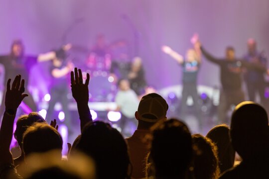 Concert Crowd with Raised Hands Under Purple Stage Lighting