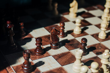 Wooden chess knight surrounded by pawns and other pieces on a chessboard. Symbol of strategy, tactical thinking, leadership, and competitive planning. © Yegor