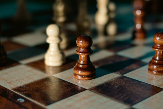 Dark wooden chess pawn in focus on a chessboard surrounded by blurred pieces. Concept of competition, leadership, strategic thinking, and business success.