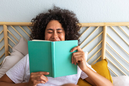 Woman enjoying leisure time reading book in bed laughing