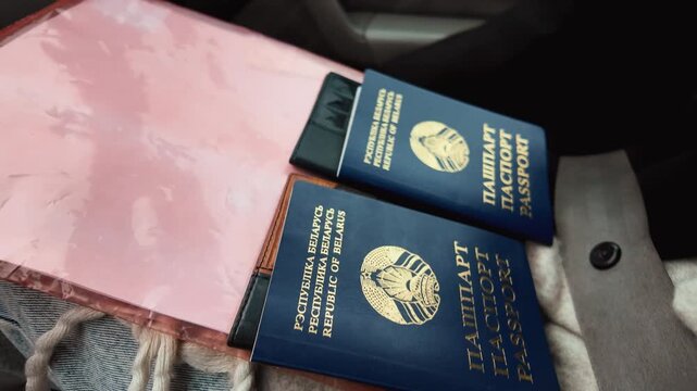 Two blue belarusian passports with a golden emblem lying on a person's lap inside a car, prepared for a journey, customs control, or border crossing with a seatbelt visible nearby